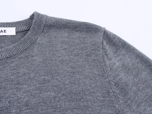 Détail d'un pull en maille grise avec col rond côtelé et étiquette de marque AE