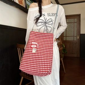 Close-up of red and white plaid tote bag with decorative Good Good label detail