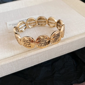 Close-up of gold elastic bracelet featuring engraved round discs on white and black box