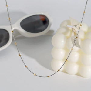 Minimalist 18k silver chain necklace with small gold bead accents on a white background