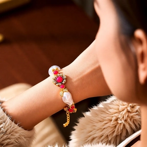 Detail eines Vintage Blumenarmbands mit roten Edelsteinen und Barockperlen am Handgelenk