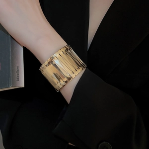 Detail of wide gold ribbed cuff bracelet worn with a professional black blazer
