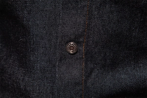 Macro shot of dark blue denim texture with yellow stitching and metal fashion button