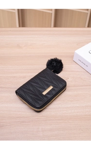Detail of black quilted leather coin purse with gold metal trim and fuzzy pom-pom charm