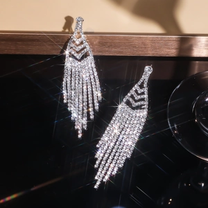 Macro detail of silver tassel earrings with sparkling rhinestones on black background