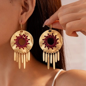 Gros plan de boucles d'oreilles bohèmes dorées avec tissage rouge et franges