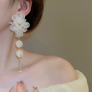 Close-up of translucent white acrylic flower tassel earrings worn by a female model