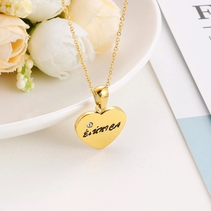 Macro detail of gold heart pendant necklace featuring a small crystal and engraved text