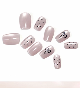 Detail of nude pink cat eye press-on nails with black polka dots and pearl bows