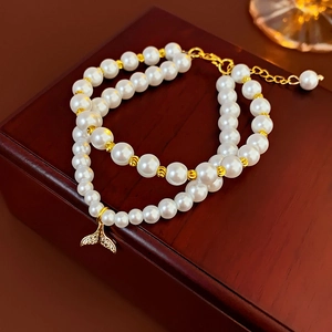 Detail of double-layer pearl bracelet with gold fish tail charm on a wooden box