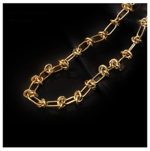 Close-up of 18K gold knot thorn chain necklace on black leather background
