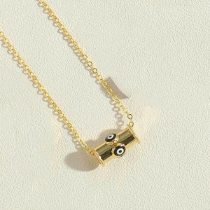 Detail of gold cylinder pendant with evil eye patterns on a fine link chain necklace