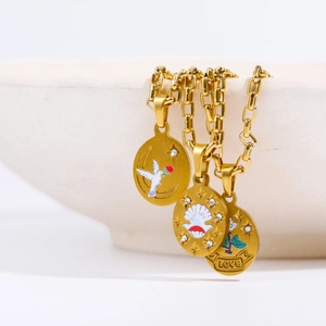 Close-up of three gold pendant necklaces with floral and dove designs on a ceramic bowl
