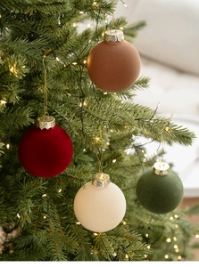Detail of 8cm flocked Christmas balls in burgundy and brown hanging on a lighted tree