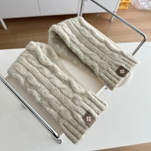 Close-up of oatmeal cable-knit leg warmer with premium leather logo tag on metal stand