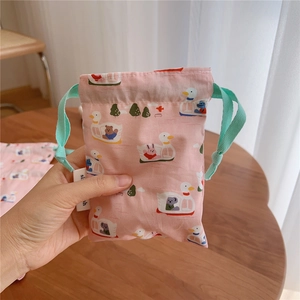 Close-up of pink cotton drawstring bag with cartoon duck prints held in hand over wooden table