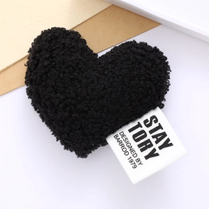 Detail shot of a black plush heart accessory with a designer fabric label on white background