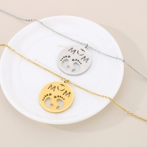Detailed view of gold and silver MOM pendants with baby footprints on a ceramic dish