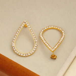 Macro shot of gold teardrop earrings with full white rhinestone pavé setting on white base