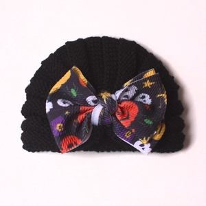 Detail of baby knit hat with Halloween pumpkin and ghost bow pattern on black fabric
