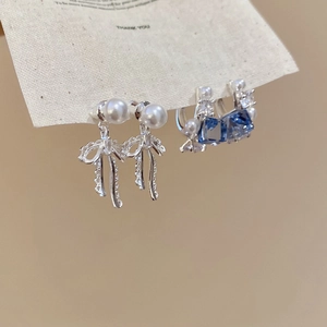 Detail of silver bow earrings with white pearl and blue square zircon on display card