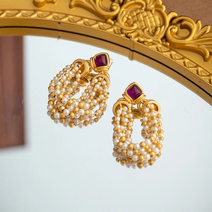 Vintage style gold earrings with purple gemstone and layered pearls on a mirror