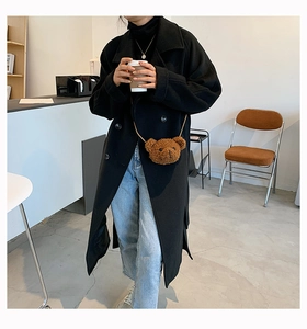 Brown plush bear crossbody bag styled with black wool coat and blue jeans in a cafe