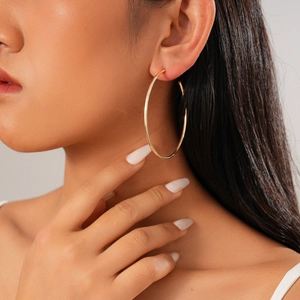Close-up of a large smooth golden geometric round hoop earring worn by a model