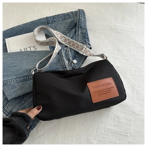 Close-up of black nylon crossbody bag with wide geometric strap and leather logo tag
