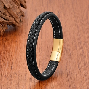 Detail of black braided leather bracelet with a polished gold magnetic clasp on wood