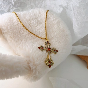 Détail du pendentif croix dorée vintage avec pierres rouges et diamants sur chaîne