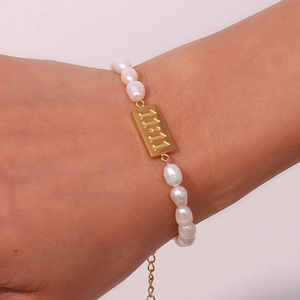Detail of freshwater pearl bracelet featuring a gold plate with 11:11 engraving on wrist