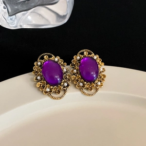 Macro detail of vintage gold flower earrings with purple oval stone and pearls on porcelain