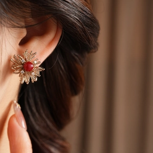 Close-up of gold flower stud earring with red gemstone and zircon on female ear