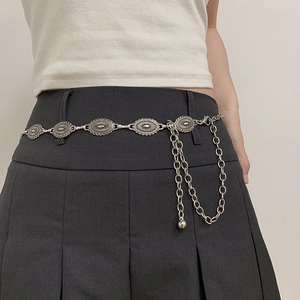 Détail d'une ceinture chaîne en métal argenté avec breloques florales et chaînes drapées