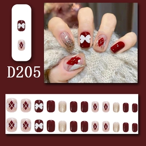 Detail of red press-on nails featuring 3D white bows, red plaid, and gold glitter designs