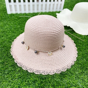 Détail d'un chapeau de paille avec bordure en dentelle, coquillages et perles mauves