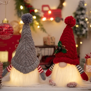 Close-up of glowing Christmas gnomes with grey and red knitted hats on wooden table