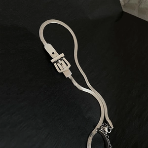 Detail shot of silver snake chain necklace featuring a belt buckle design on black surface