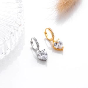 Detail of gold and silver heart-shaped zircon earrings with small stones on the hoops