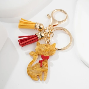 Close-up of golden cat keychain with yellow acrylic pendant and red tassel charms