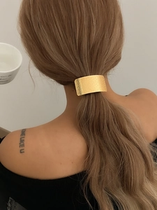 Detail of a textured golden rectangular metal hair clip securing a ponytail on model