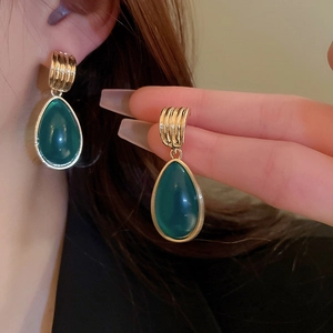 Close-up of vintage gold-textured earrings with green teardrop gemstones on model