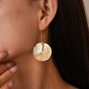 Close-up of golden geometric earrings with textured circular pattern worn by a model