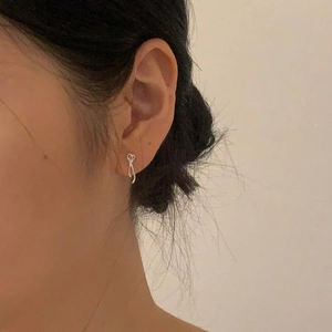 Close-up of a minimalist silver knot stud earring worn on a model's ear for casual style