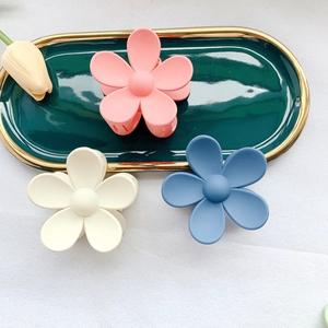 Detailed top view of three matte flower hair claw clips in pastel colors on a green tray