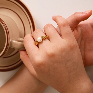 Elegant gold twisted croissant ring with pearl detail worn by a model holding a cup