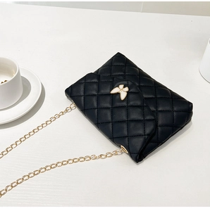 Detail of black quilted shoulder bag featuring gold chain strap and butterfly clasp detail