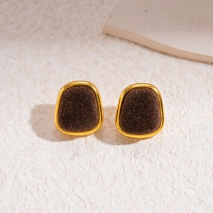 Detail of round brown flocked earrings with gold metal frame on a textured surface