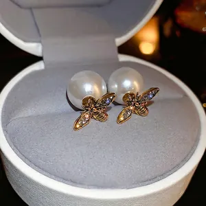 Elegant gold bee stud earrings with white pearl and sparkling crystals on jewelry case